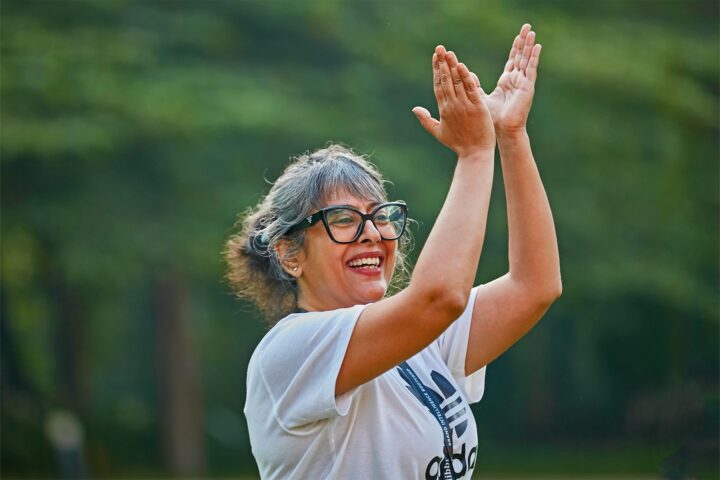 A participant outdoors, hands raised together, smiling