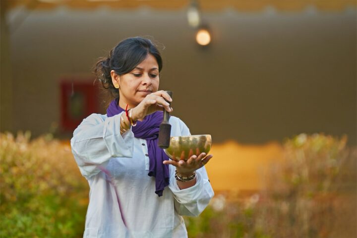 A facilitator holding a singing bowl outdoors in late afternoon light