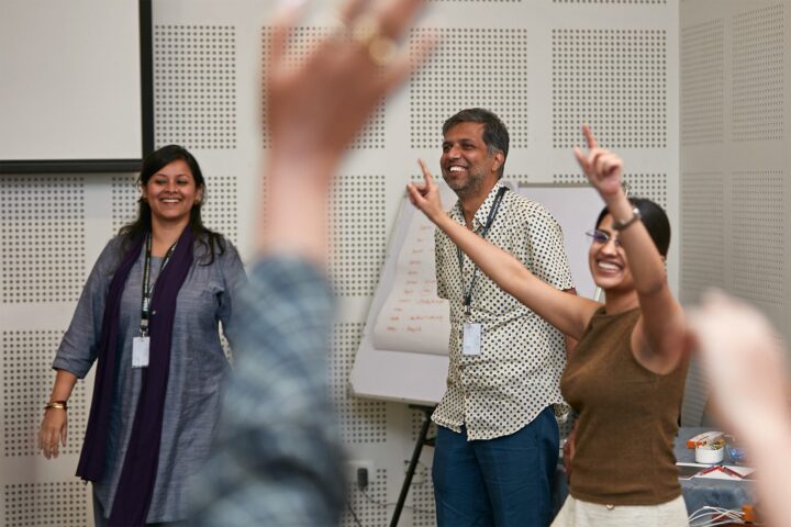 Participants indoors with arms raised, a facilitator leading from the left