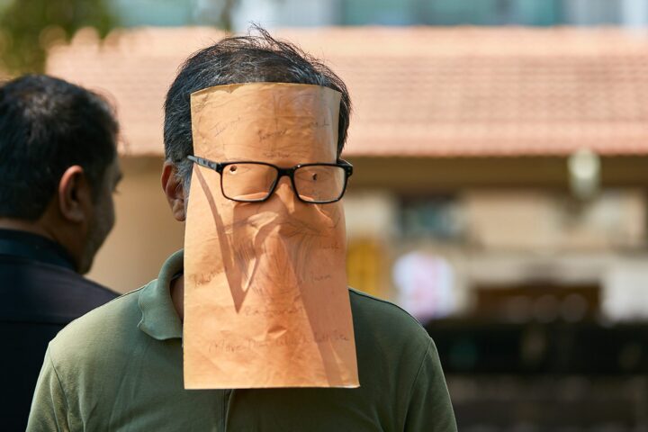 A participant wearing a paper bag with glasses drawn on it