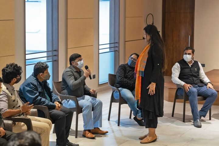 A facilitator holding a microphone, speaking to participants seated in a circle