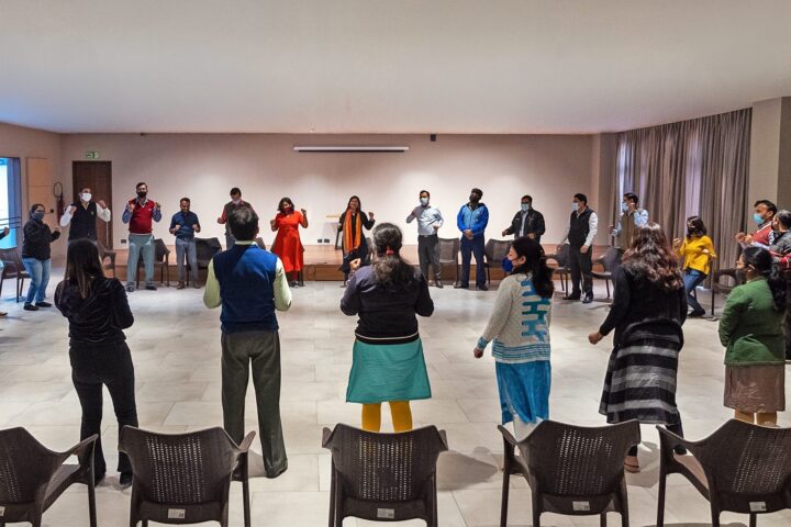 Participants standing in a wide circle in the hall, chairs pushed back behind them
