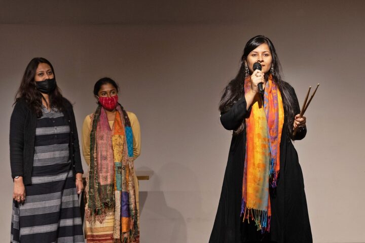 A facilitator on the stage with a microphone, two participants standing beside her