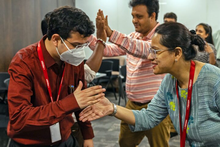Two participants facing each other with palms raised and touching, a third looking on