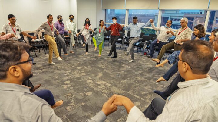A wide view of the room, participants seated and standing in a large circle