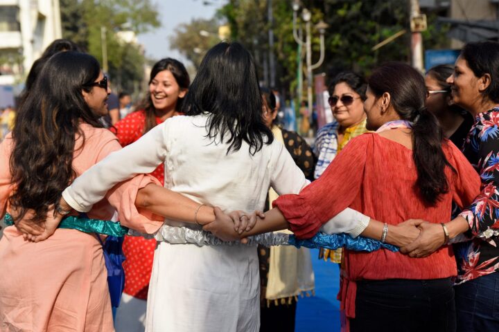 Women standing in a close ring on the street, arms crossed and hands joined, laughing