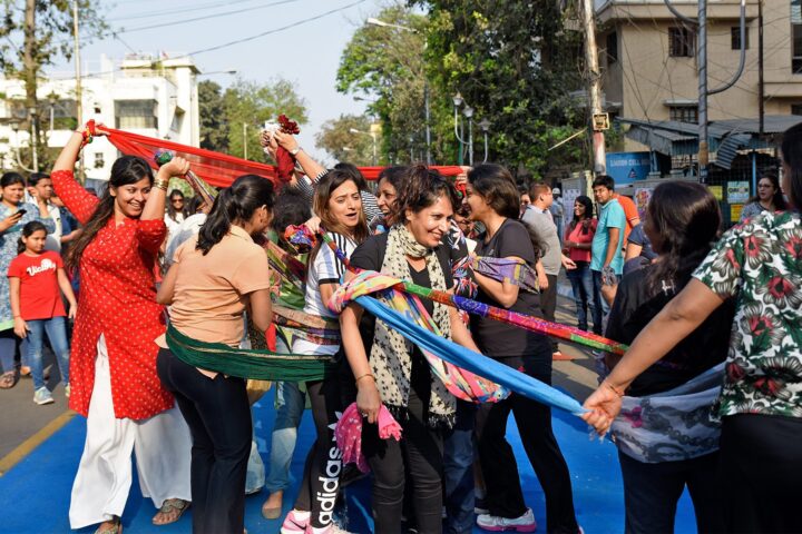 Women holding a long band of knotted coloured scarves above their heads