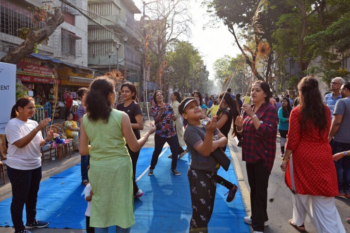 A wide view down the closed road, a group moving together on a blue mat with onlookers around them