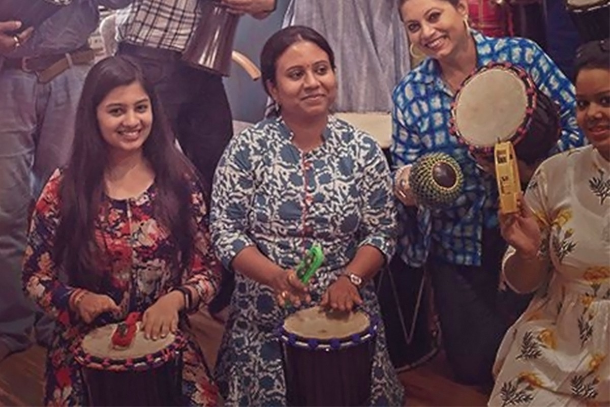 A group holding djembes, a frame drum and shakers during a drum circle session, smiling towards the camera.