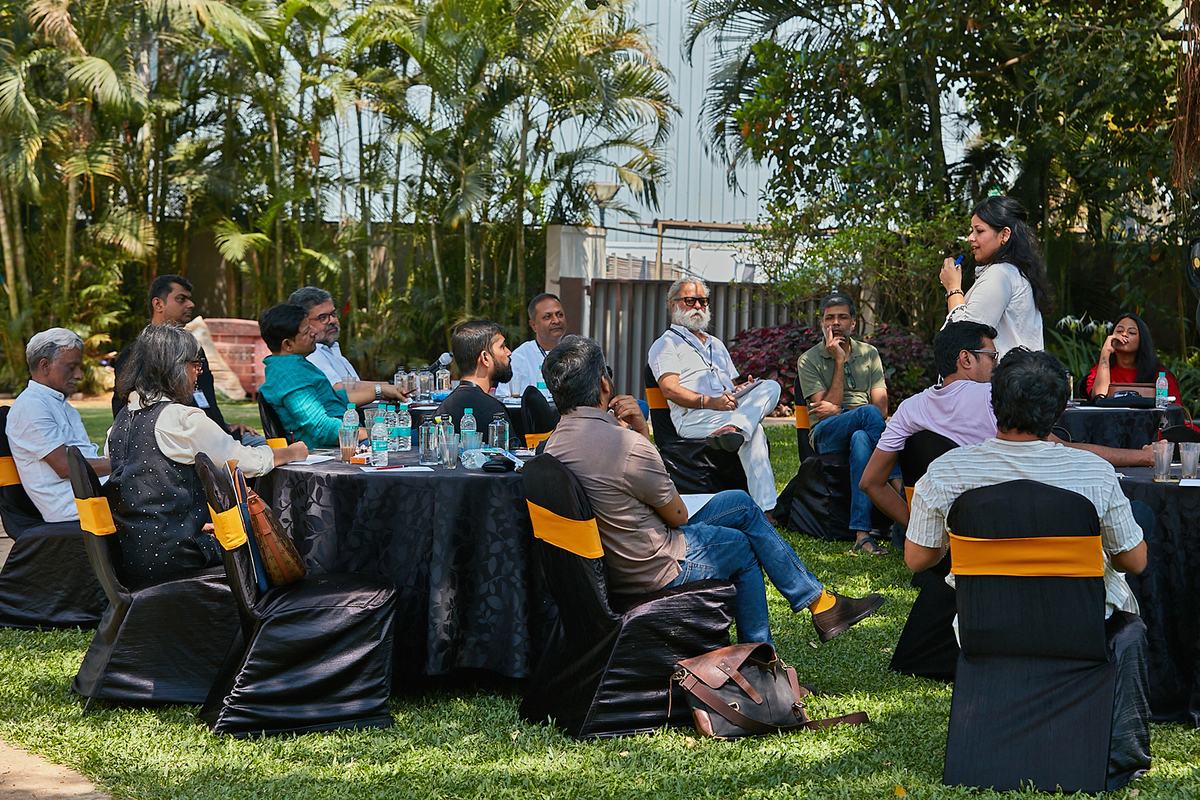 Delegates seated around round tables on grass at an outdoor corporate offsite, palms and greenery behind.