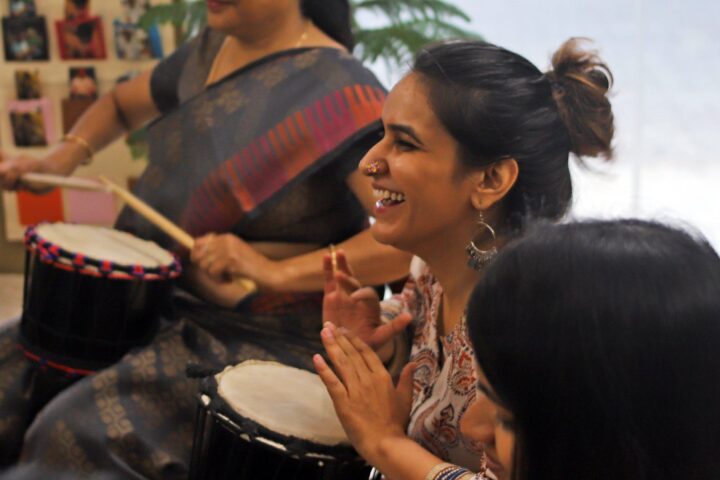 A participant laughing mid-clap, another drumming behind her