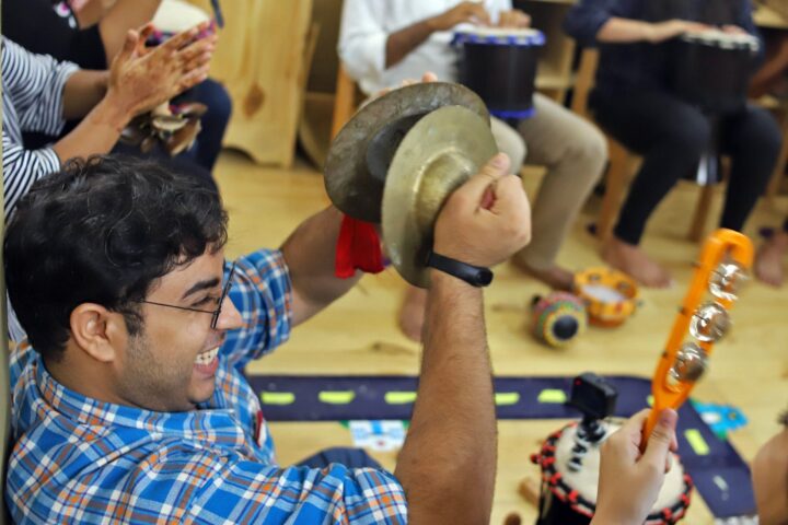 A participant raising a pair of brass cymbals overhead, grinning