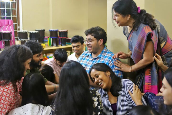 A close huddle of participants laughing together, stacked drums behind them