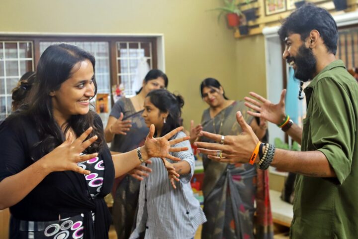 Two participants facing each other with palms raised and mirrored, others doing the same behind