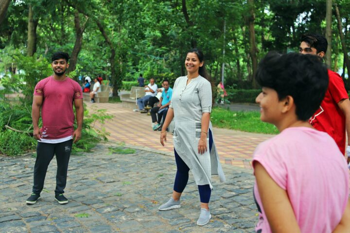 A facilitator walking a cobbled park path in the morning, participants standing among the trees around her