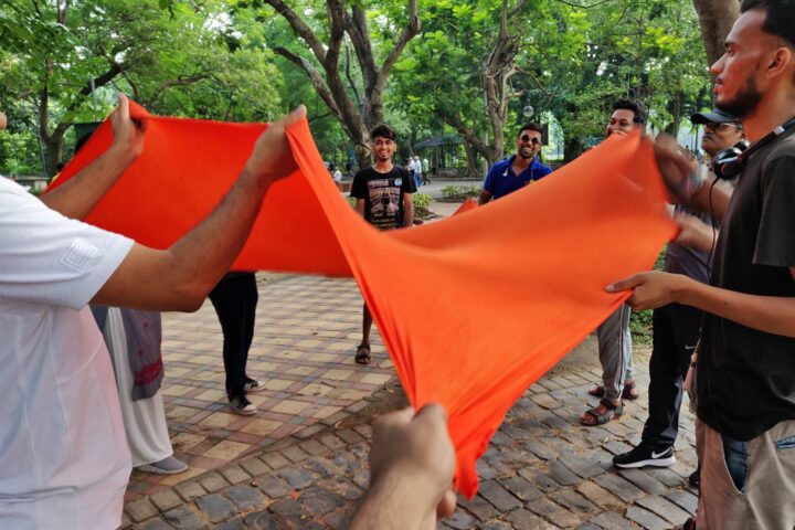A wide circle of participants pulling an orange cloth tight between them, laughing