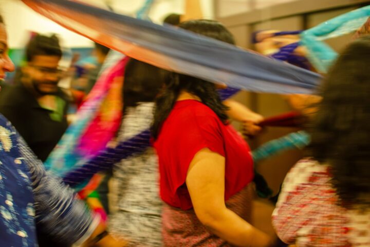 Coloured fabric strips sweeping through a group mid-movement, the room a blur of motion