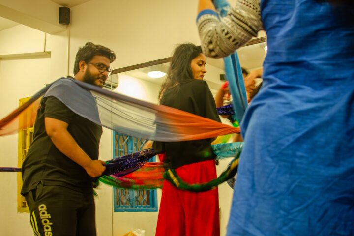 A participant lifting a length of grey cloth overhead beside a mirrored wall