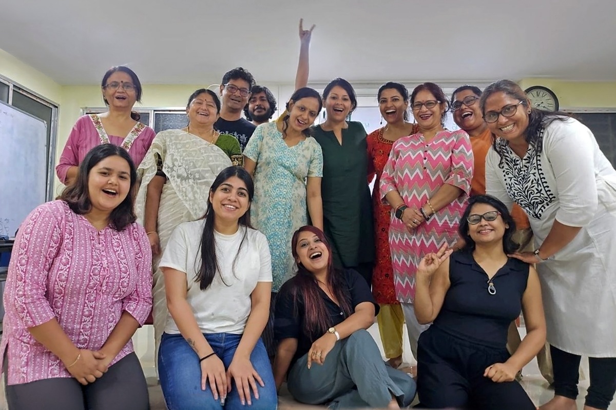 Participants laughing in a classroom with a whiteboard and a wall clock behind them, one arm raised high at the back.