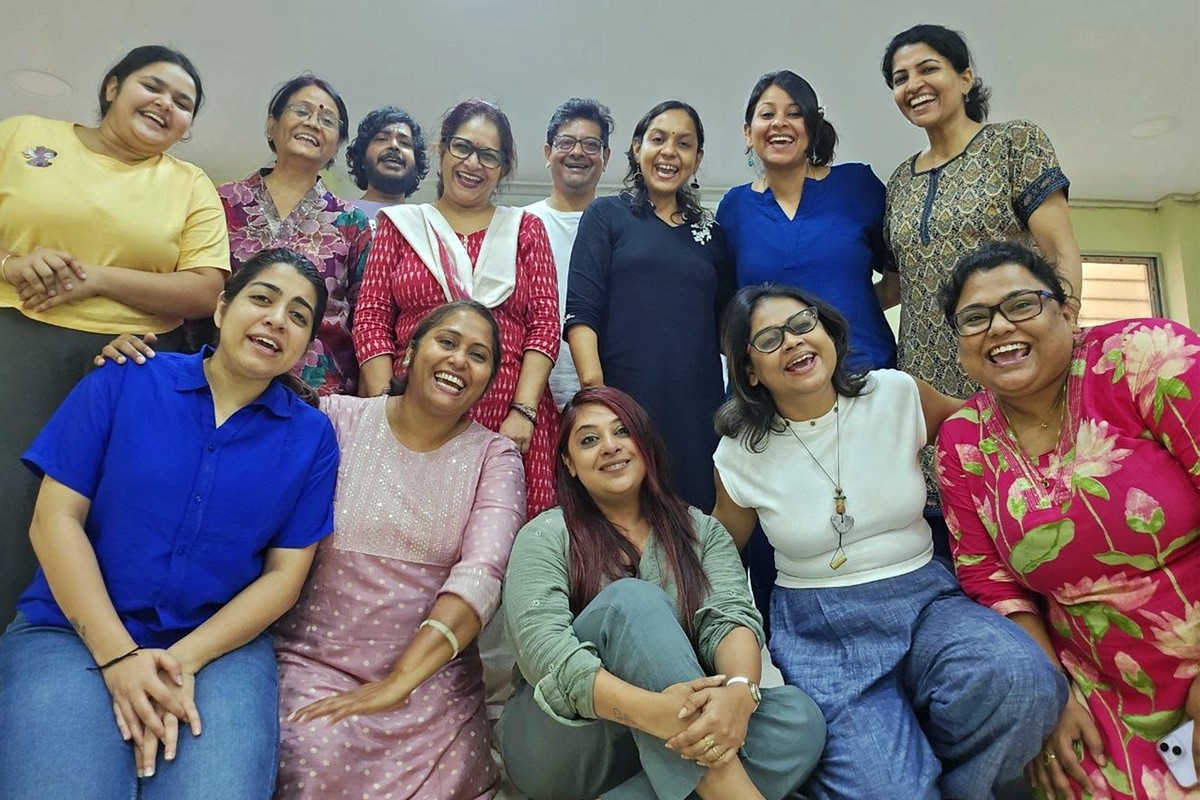 Participants photographed from a low angle, all laughing, the back row standing and the front row seated close together.